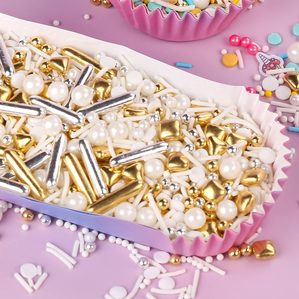 Gold, silver, and white pearl sprinkles in a pink cupcake liner on a purple background.
