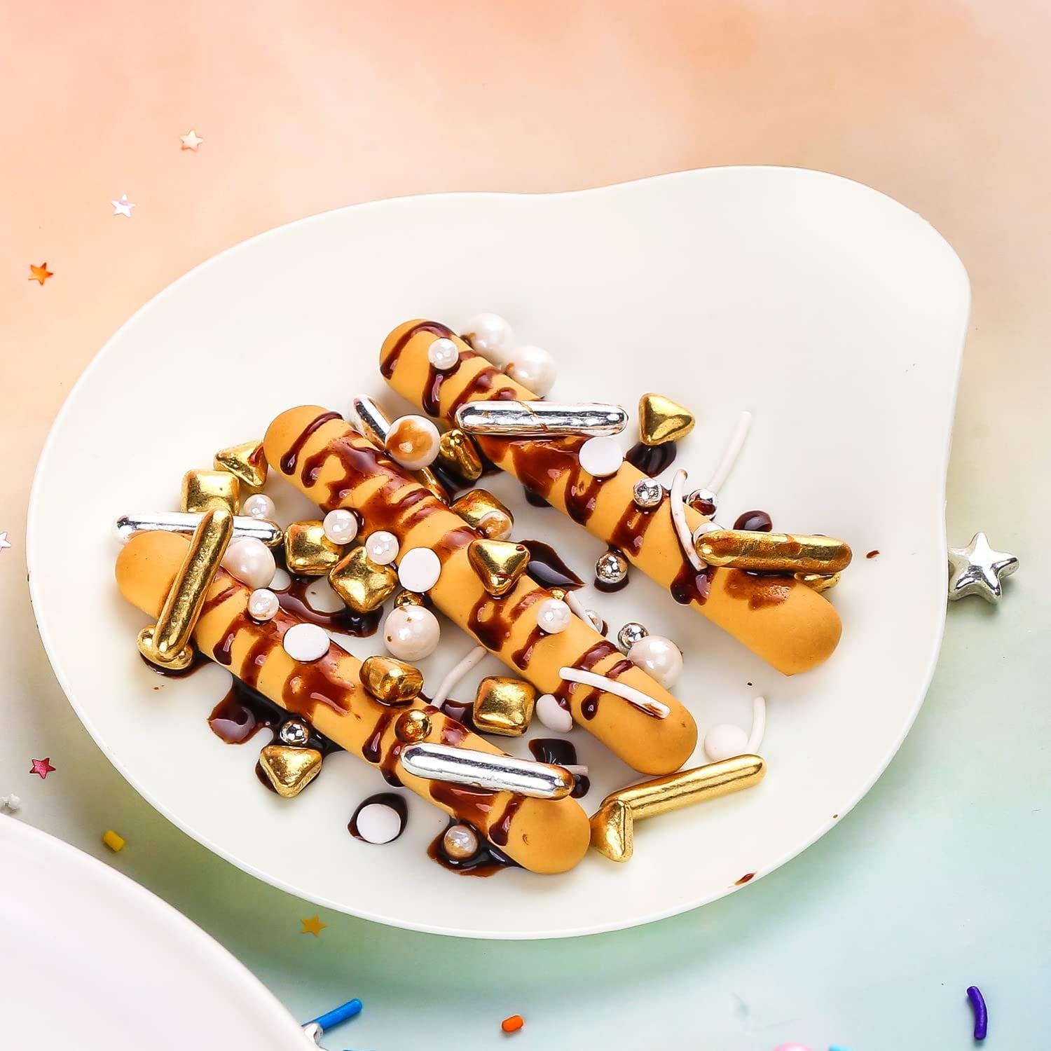 Decorated cookies with chocolate drizzle and gold, silver, and pearl sprinkles on a white plate.