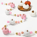 Felt pumpkin garland with pink, white, and gray pumpkins, pink and white pom-poms, and gold beads on a white background.