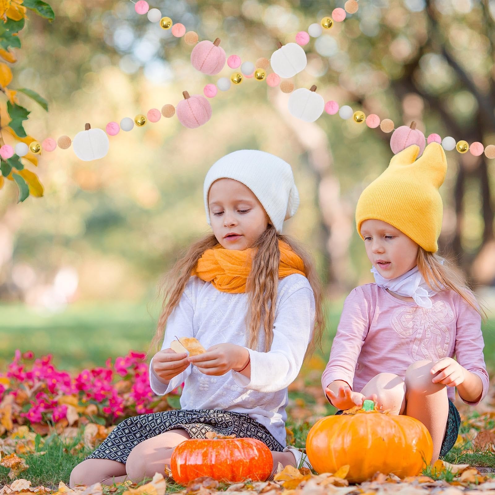 Two young girls sitting in autumn leaves with a felt pumpkin garland overhead
