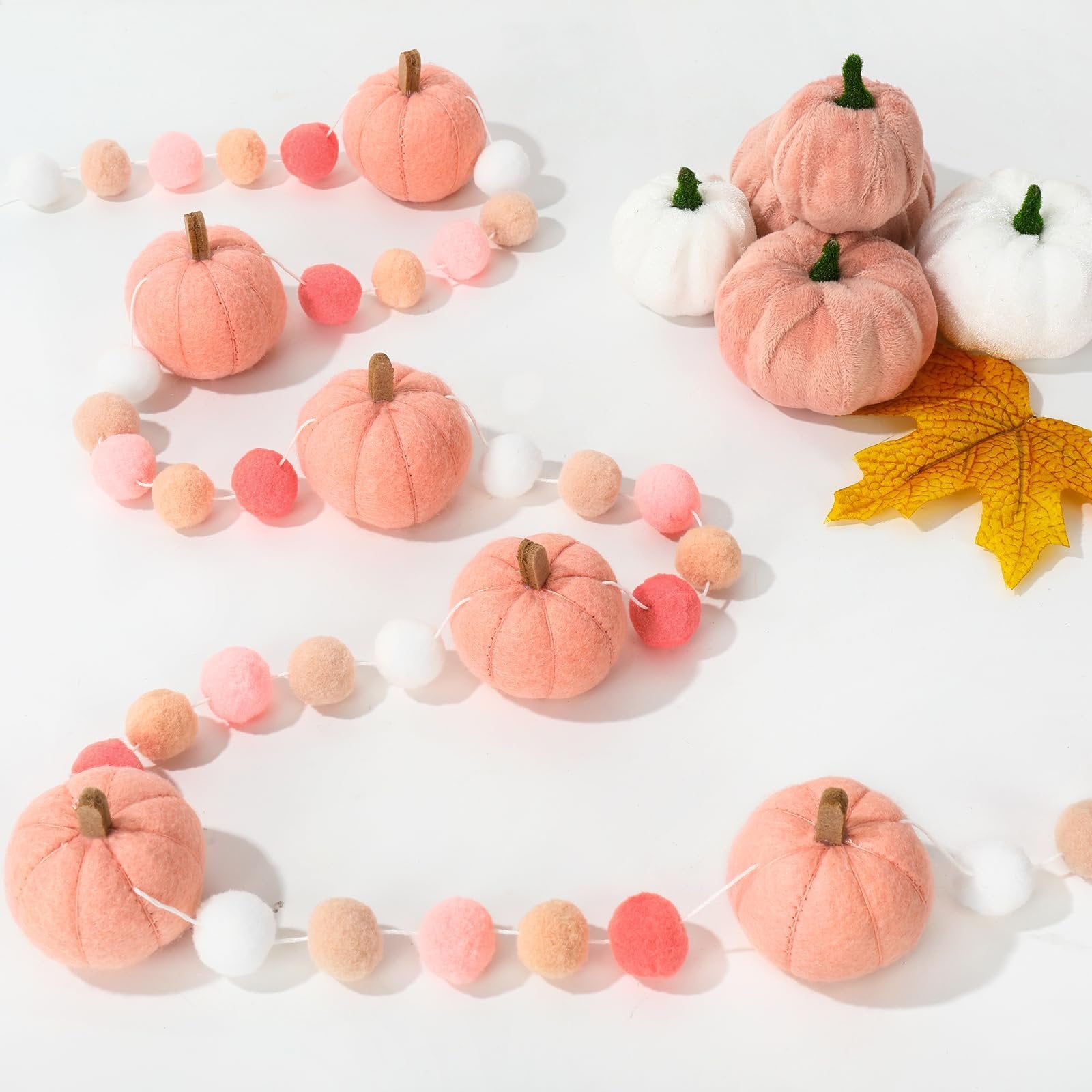 Fall felt ball garland with pink pumpkins and pom poms, arranged on a white surface with a yellow leaf.