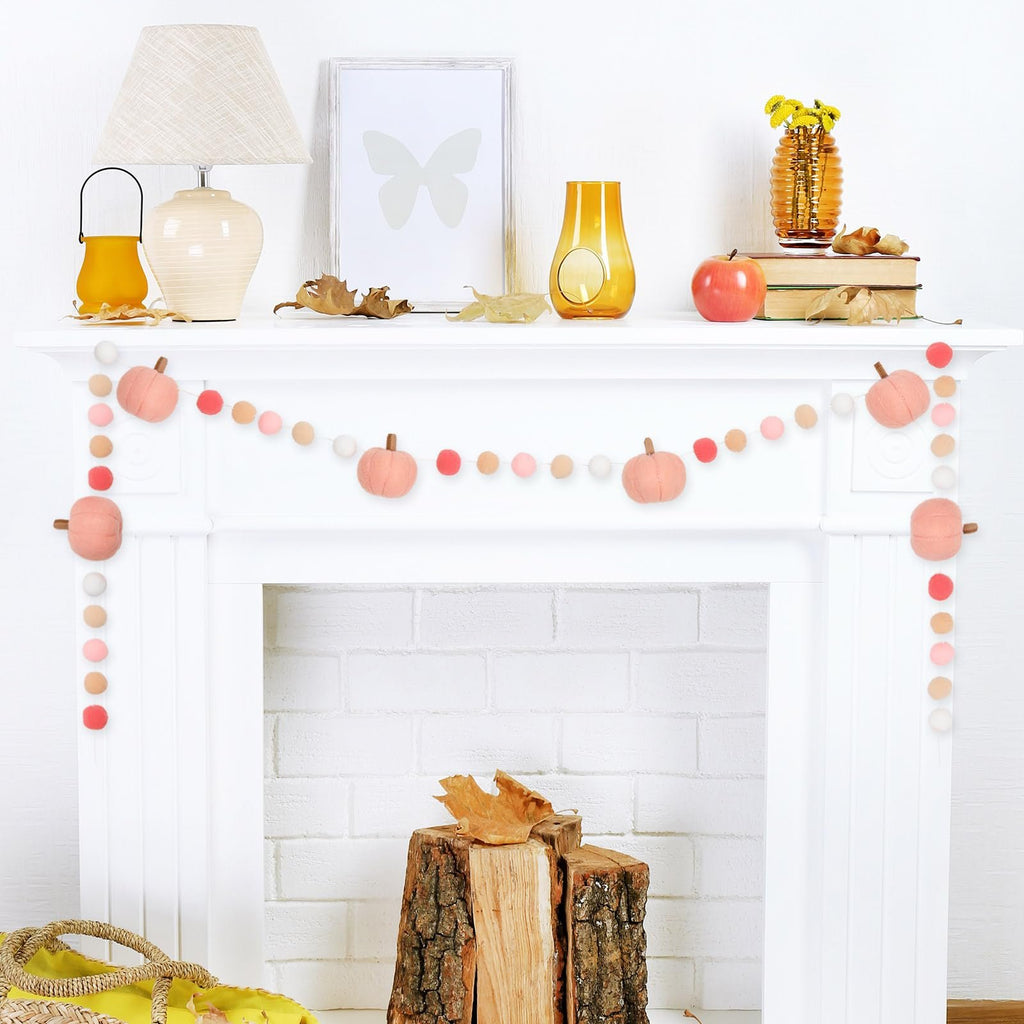 Felt ball garland with pink pumpkins and pom poms draped across a white fireplace mantel, decorated for autumn.
