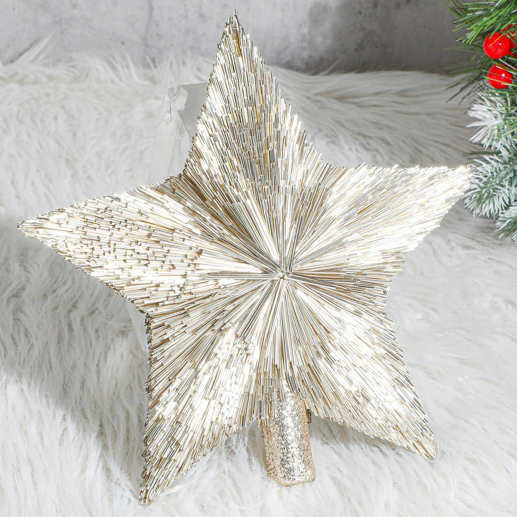 Champagne gold star tree topper with a glittery base, resting on a white fluffy surface with a hint of a Christmas tree on the right.