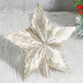 Champagne gold star tree topper with a glittery base, resting on a white fluffy surface with a hint of a Christmas tree on the right.