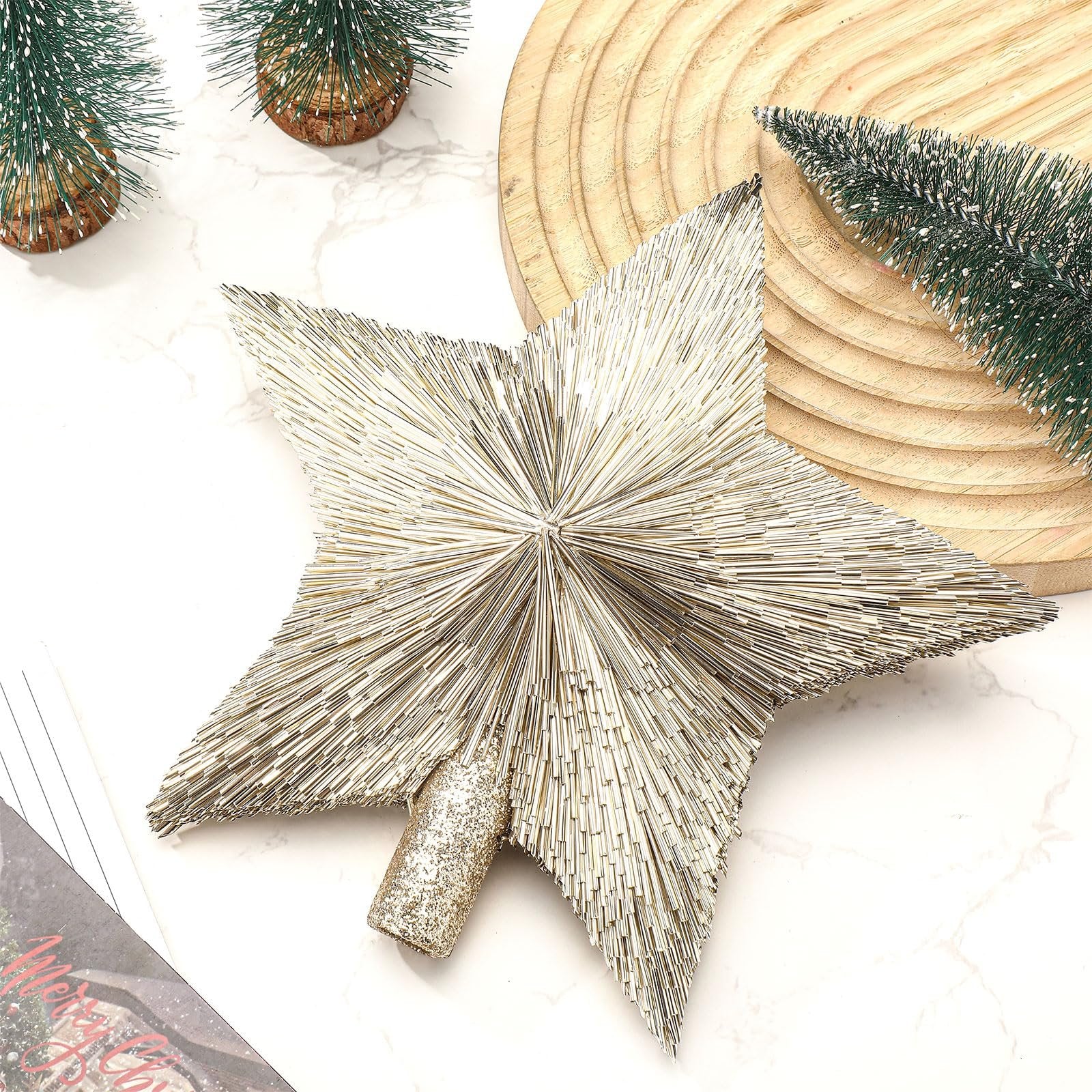 Champagne gold star tree topper with glittery base, surrounded by mini Christmas trees and wood slice.