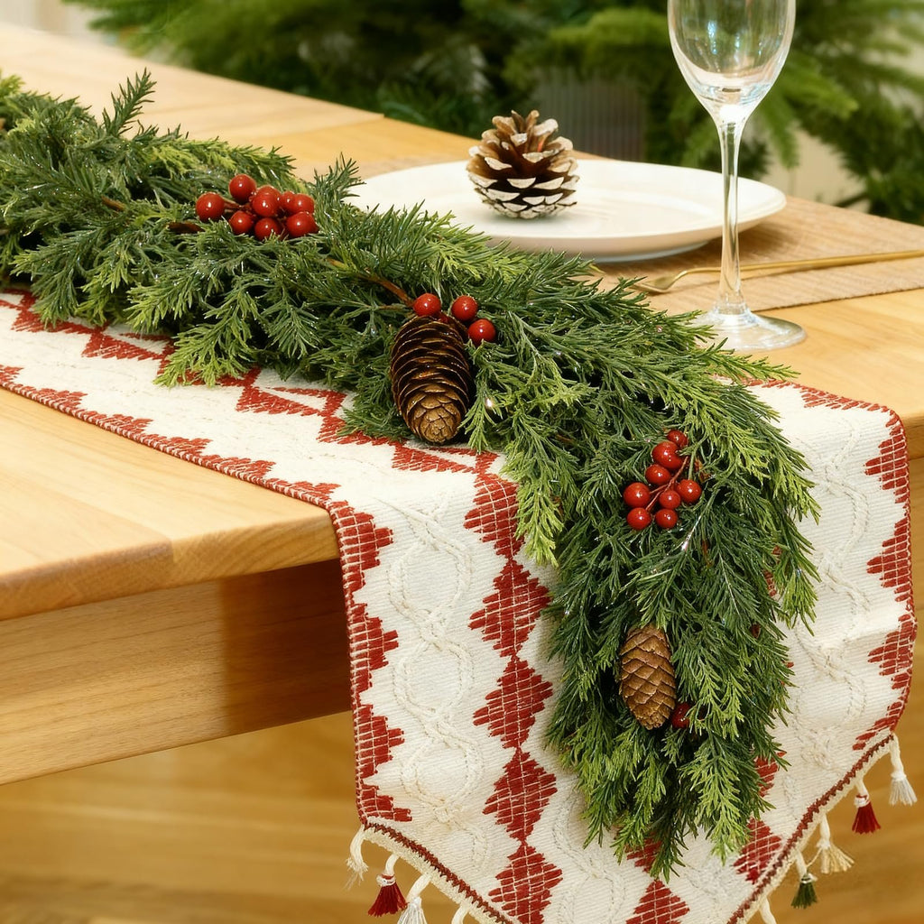 Christmas garland with pinecones and red berries draped over a table runner on a wooden table.
