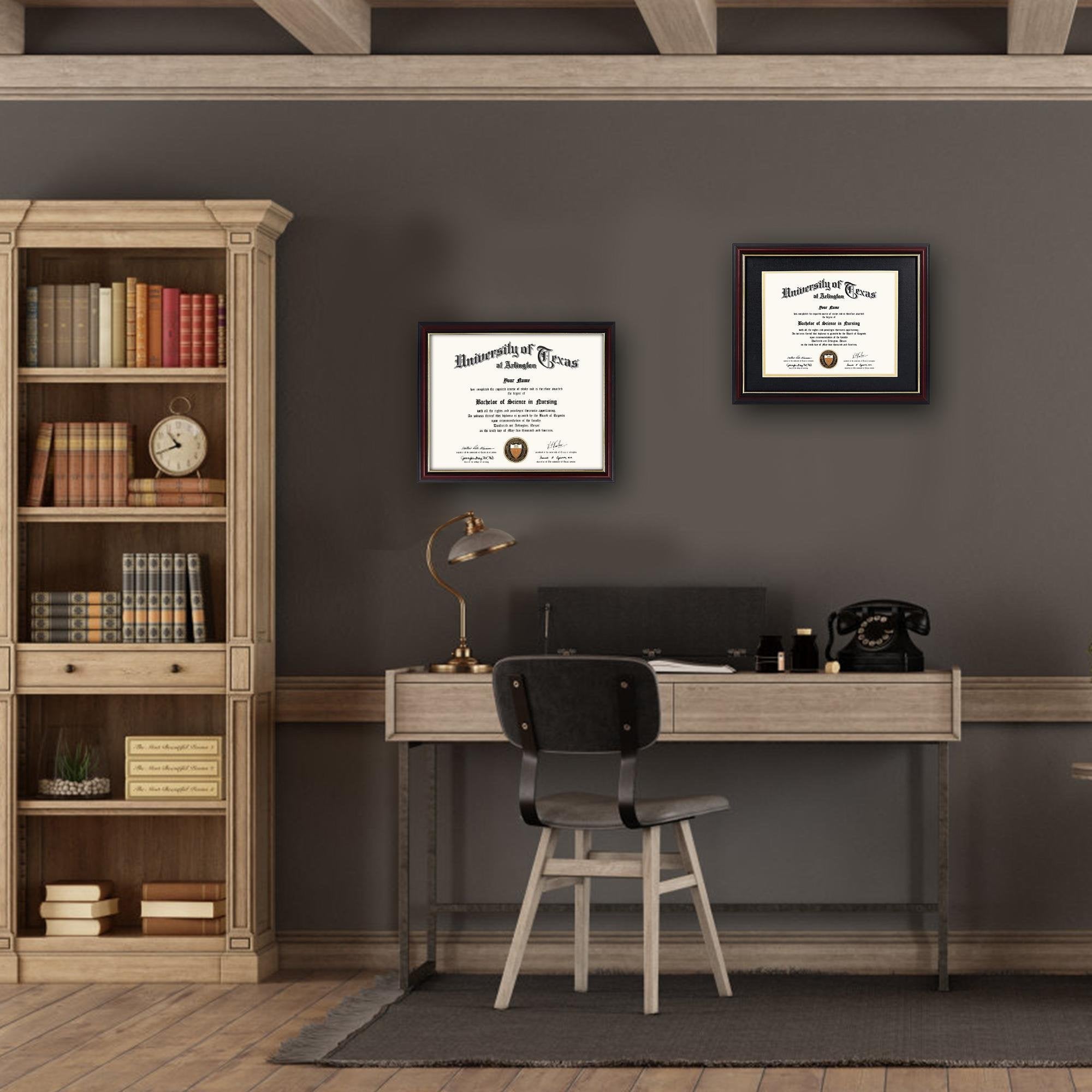 Two framed diplomas displayed on a wall above a desk in a study with a bookshelf.