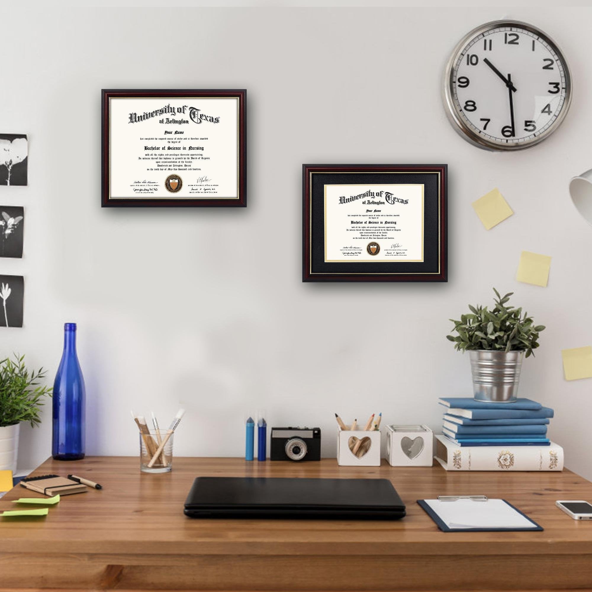 Two framed diplomas on a wall above a wooden desk with office supplies and a clock.