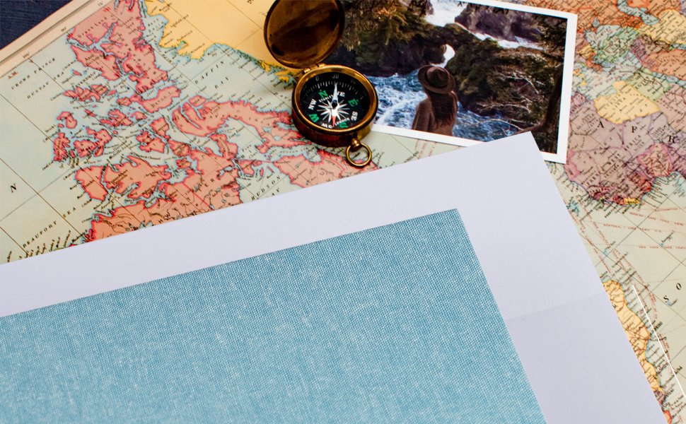 Vintage map with a compass and a photograph of a person by the sea, with blank pages and a textured blue sheet.