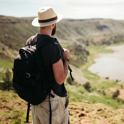 Man with backpack and hat looking out over a scenic landscape with a lake