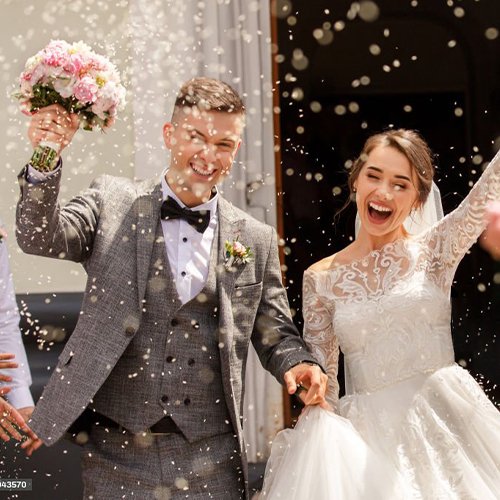 Newlyweds celebrating with confetti falling around them outside a building.