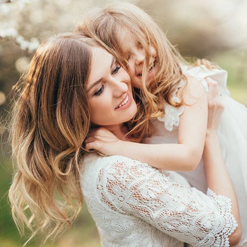 Mother and daughter embracing outdoors, both smiling and happy.