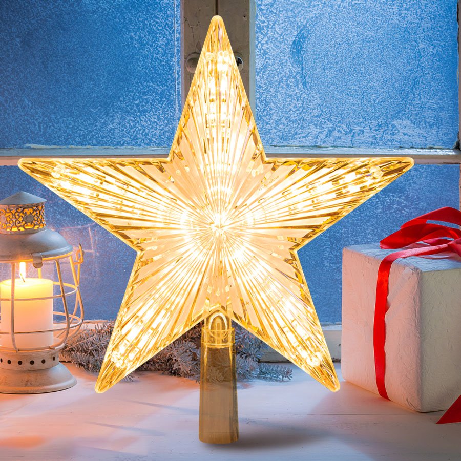 Warm white LED star tree topper with ribbed prismatic design, lit up and placed on a windowsill with a gift and lantern.