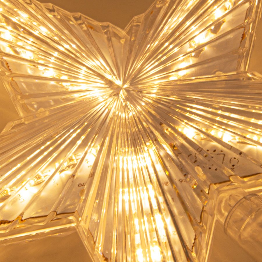 Close-up of a clear, ribbed star-shaped tree topper with warm white LED lights illuminating its prismatic design.