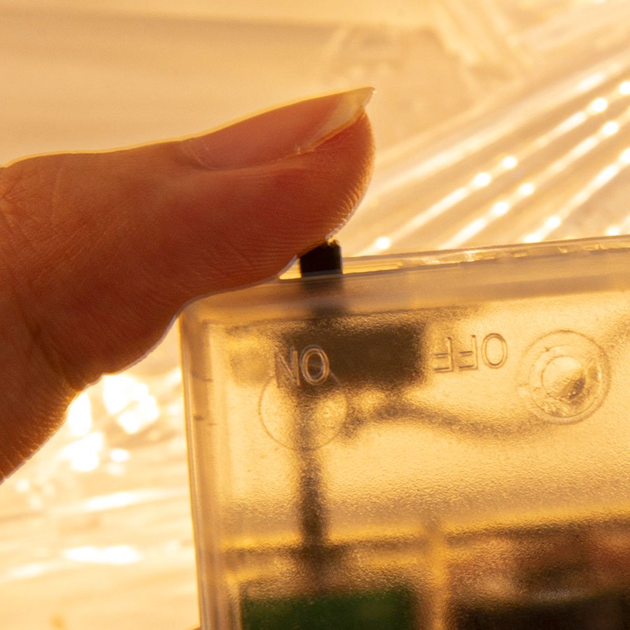 Close-up of a thumb pressing the ON/OFF switch on a clear battery pack for LED lights.