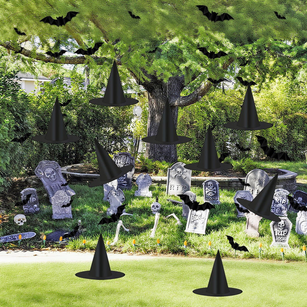 Halloween graveyard scene with black witch hats and 3D bats hanging from trees and scattered on the grass.