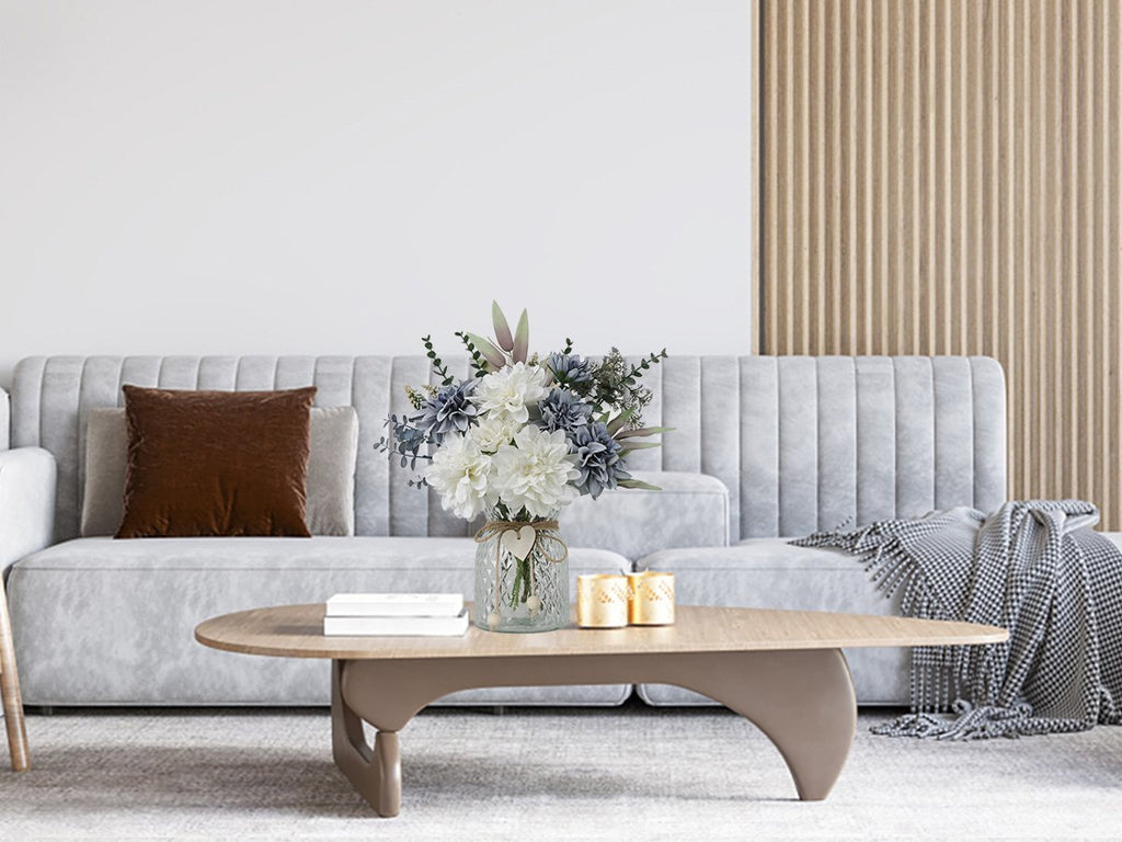 Artificial dahlia flower arrangement in a glass vase on a coffee table in a living room setting.