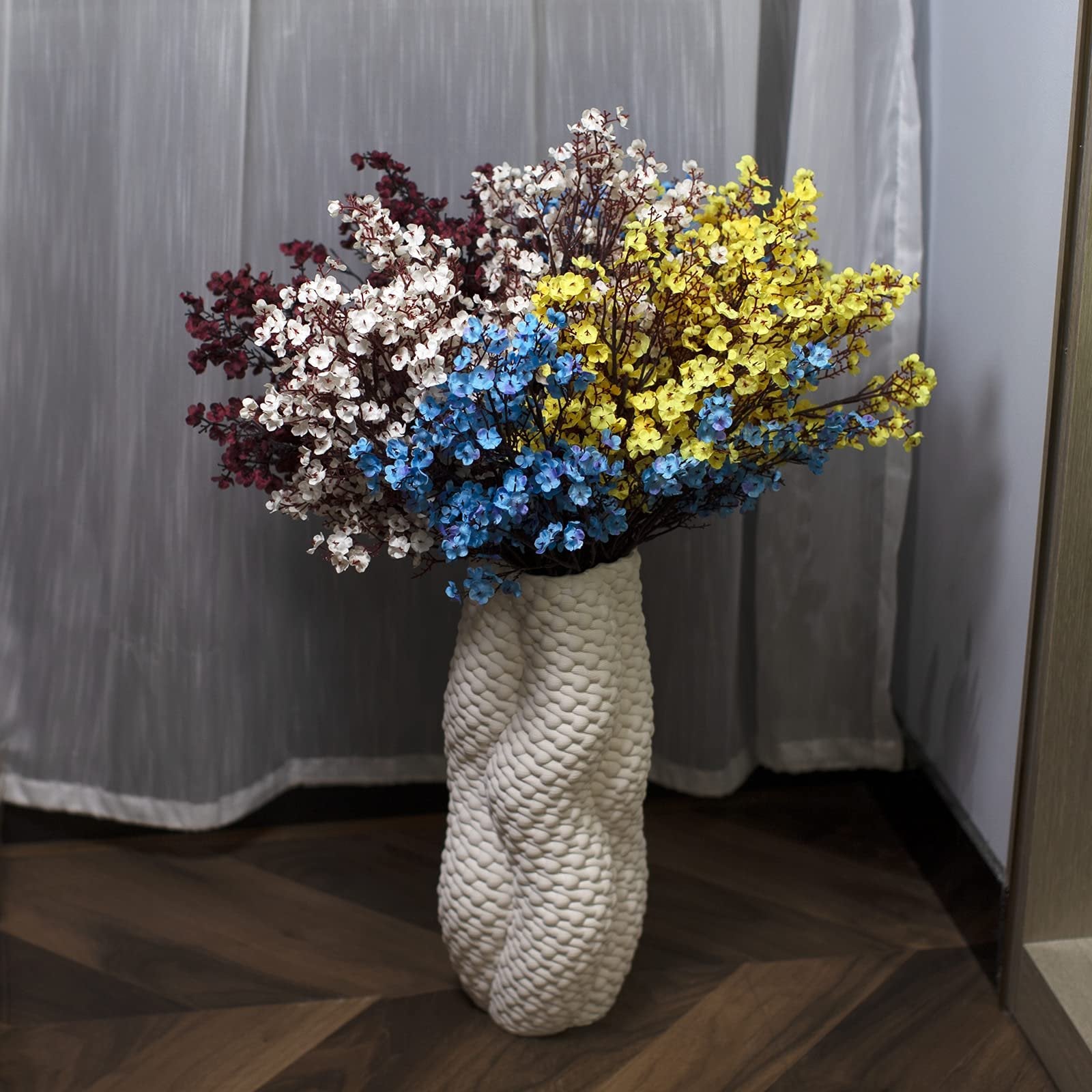 Bouquet of artificial baby's breath flowers in burgundy, white, blue, and yellow in a textured white vase.