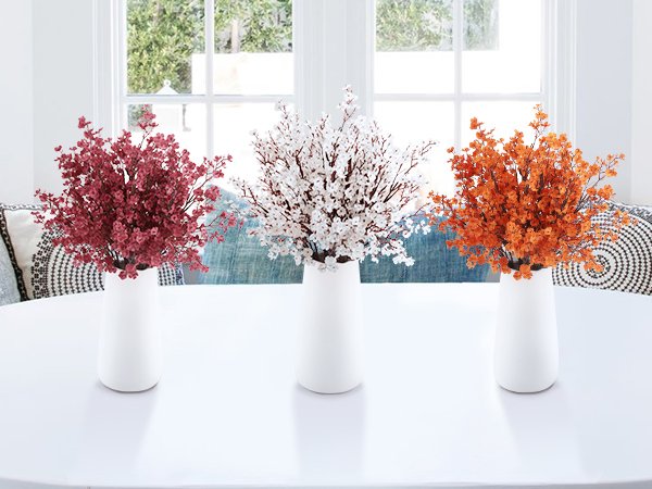 Three vases with artificial baby's breath flowers in red, white, and orange on a white table.
