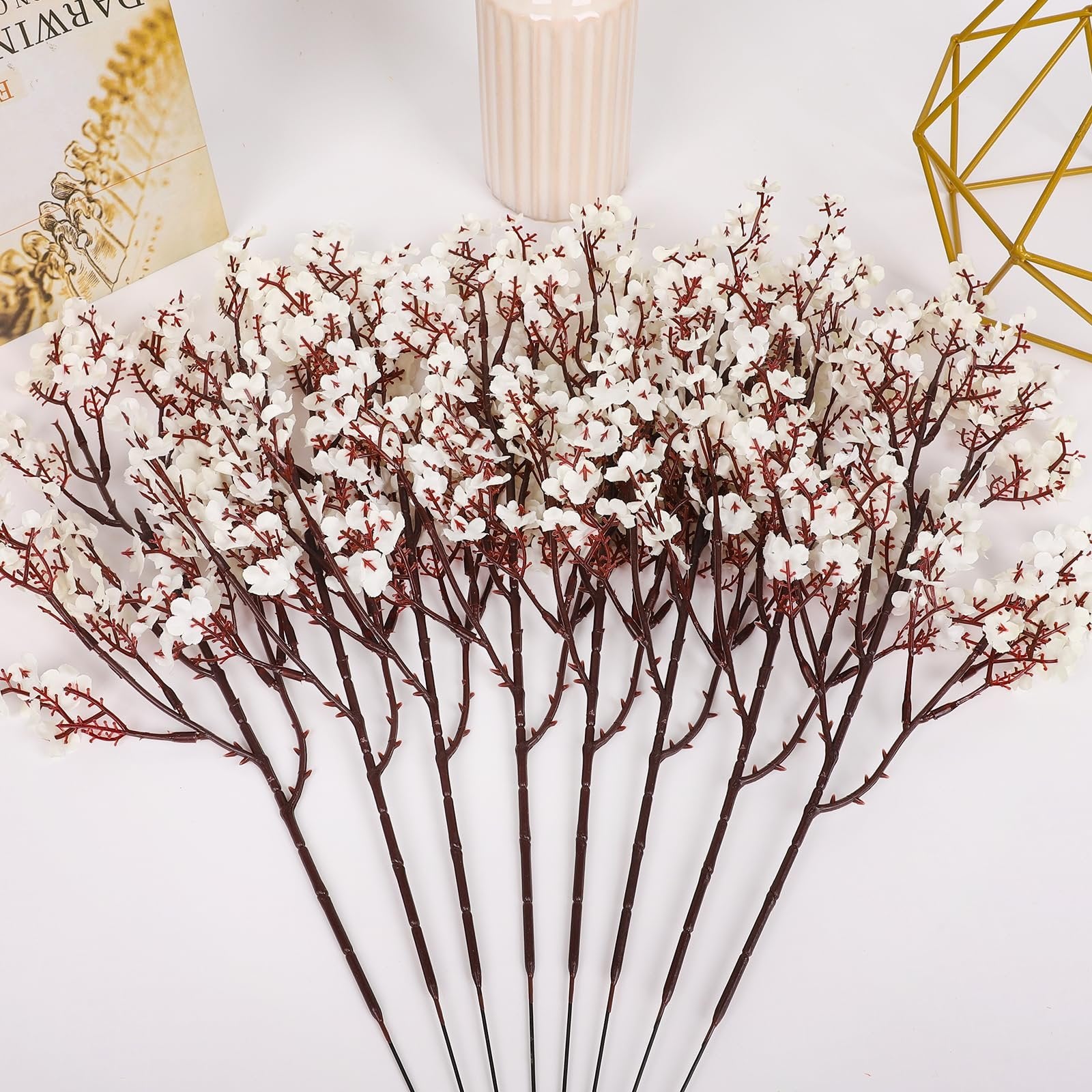 Bundle of white baby's breath artificial flowers with dark brown stems, arranged on a white surface with decorative items.