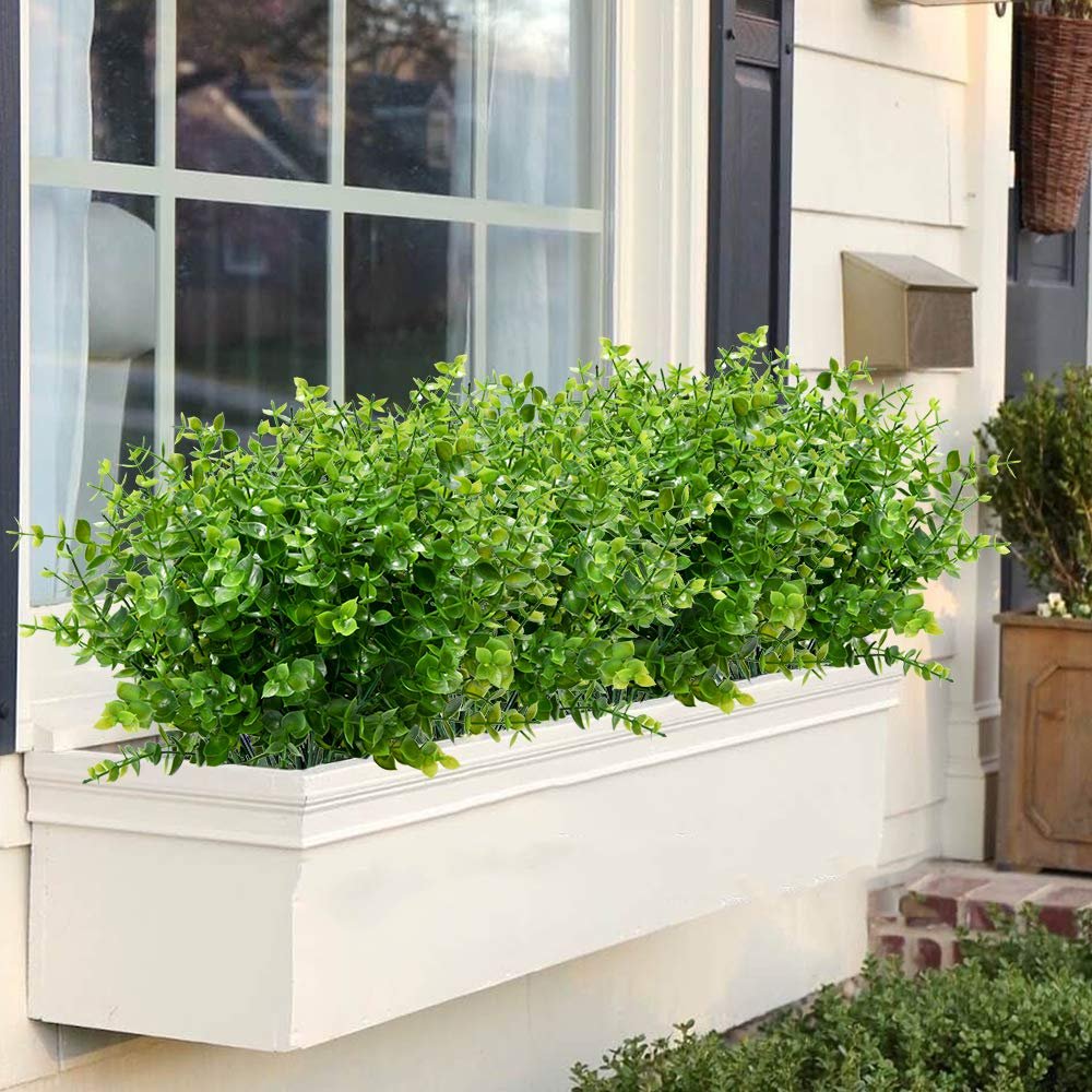 Artificial boxwood stems in a white window planter box outside a house.
