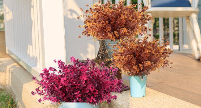 Three bundles of artificial fall flowers in magenta and brown hues, arranged on a porch with white railing.