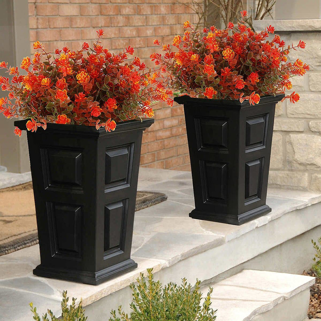 Two black planters filled with artificial orange and red fall flowers on a stone porch.