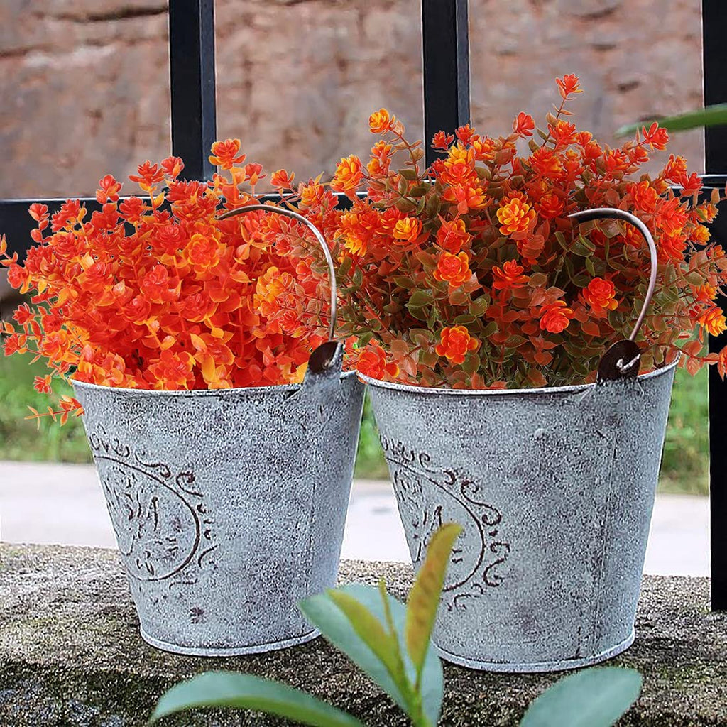 Two distressed metal buckets filled with vibrant orange and green artificial fall flowers, set outdoors.