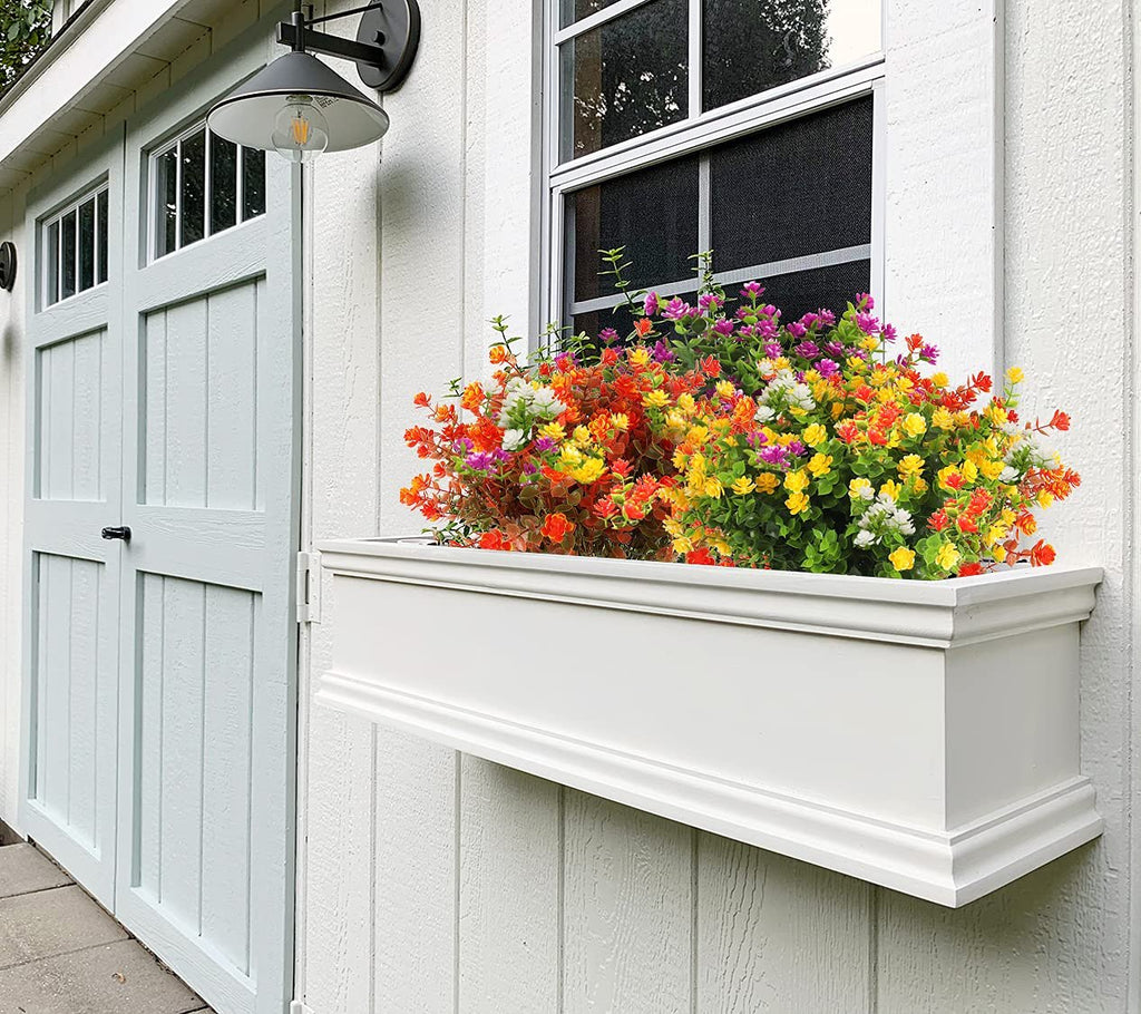 Window box filled with colorful artificial fall flowers and eucalyptus leaves mounted on a white shed wall.