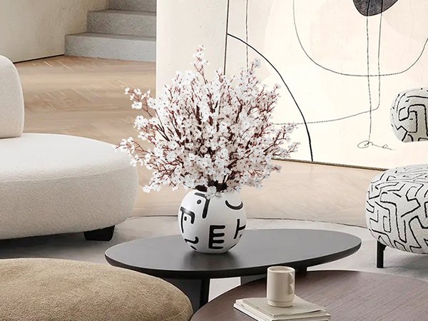 Artificial light brown gypsophila flowers in a decorative vase on a coffee table in a living room setting.