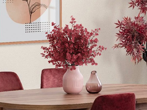 Pink vase with red artificial flowers on a wooden table with chairs and abstract art