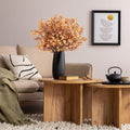 Light brown artificial gypsophila flowers in a black vase on a wooden coffee table, next to a sofa and framed art.