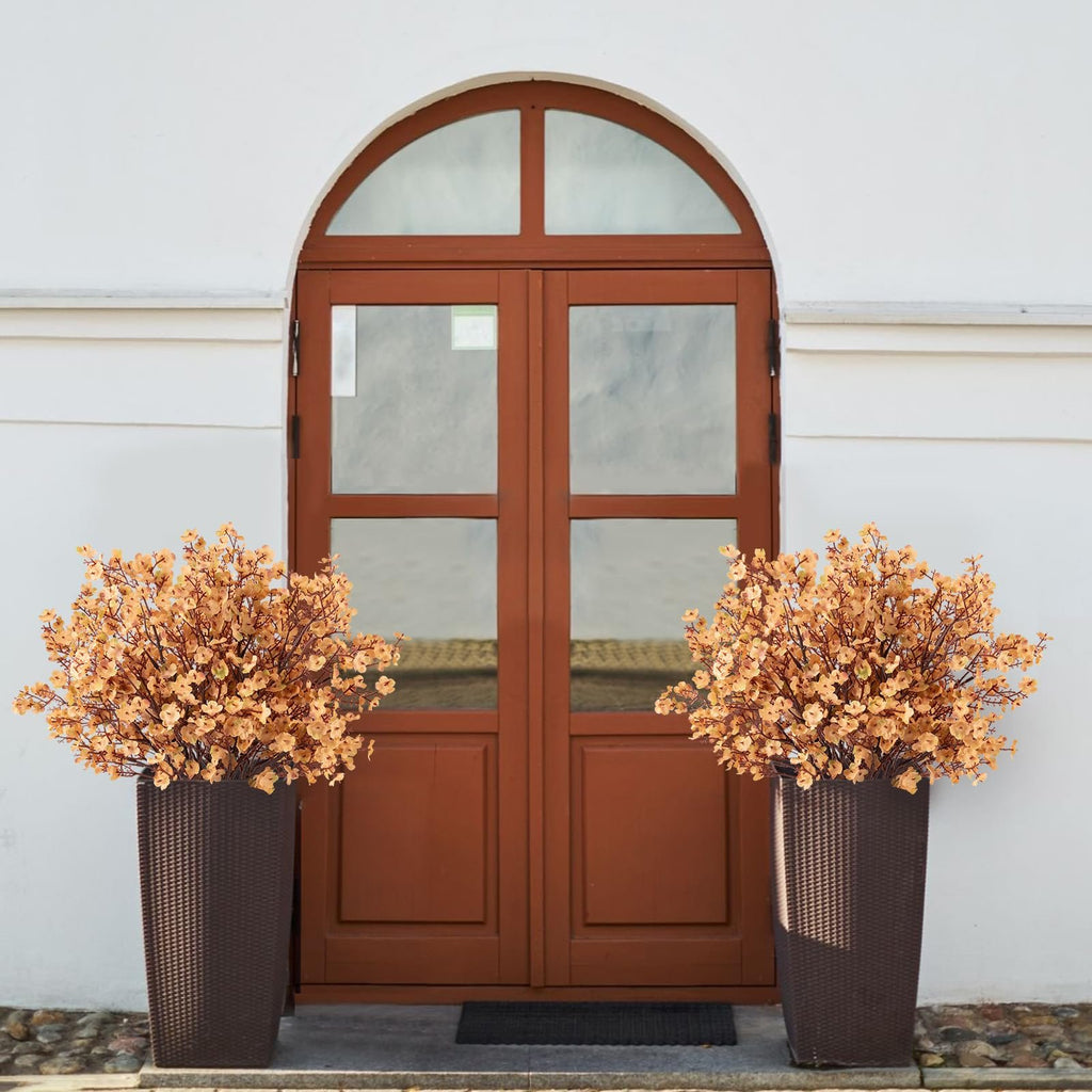 Two tall brown planters filled with light brown artificial gypsophila flowers flanking a wooden arched door.