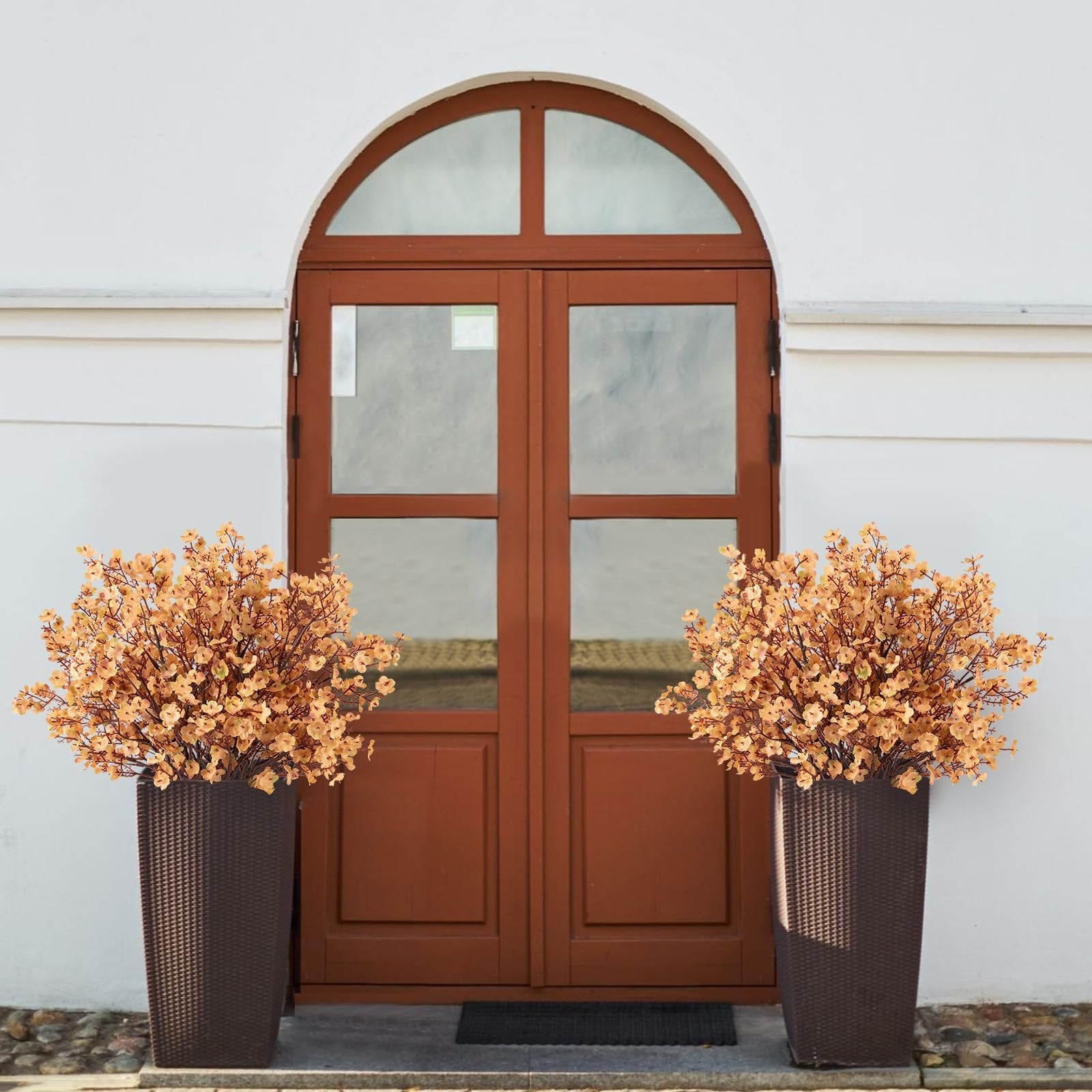 Two tall brown planters filled with light brown artificial gypsophila flowers flanking a wooden arched door.