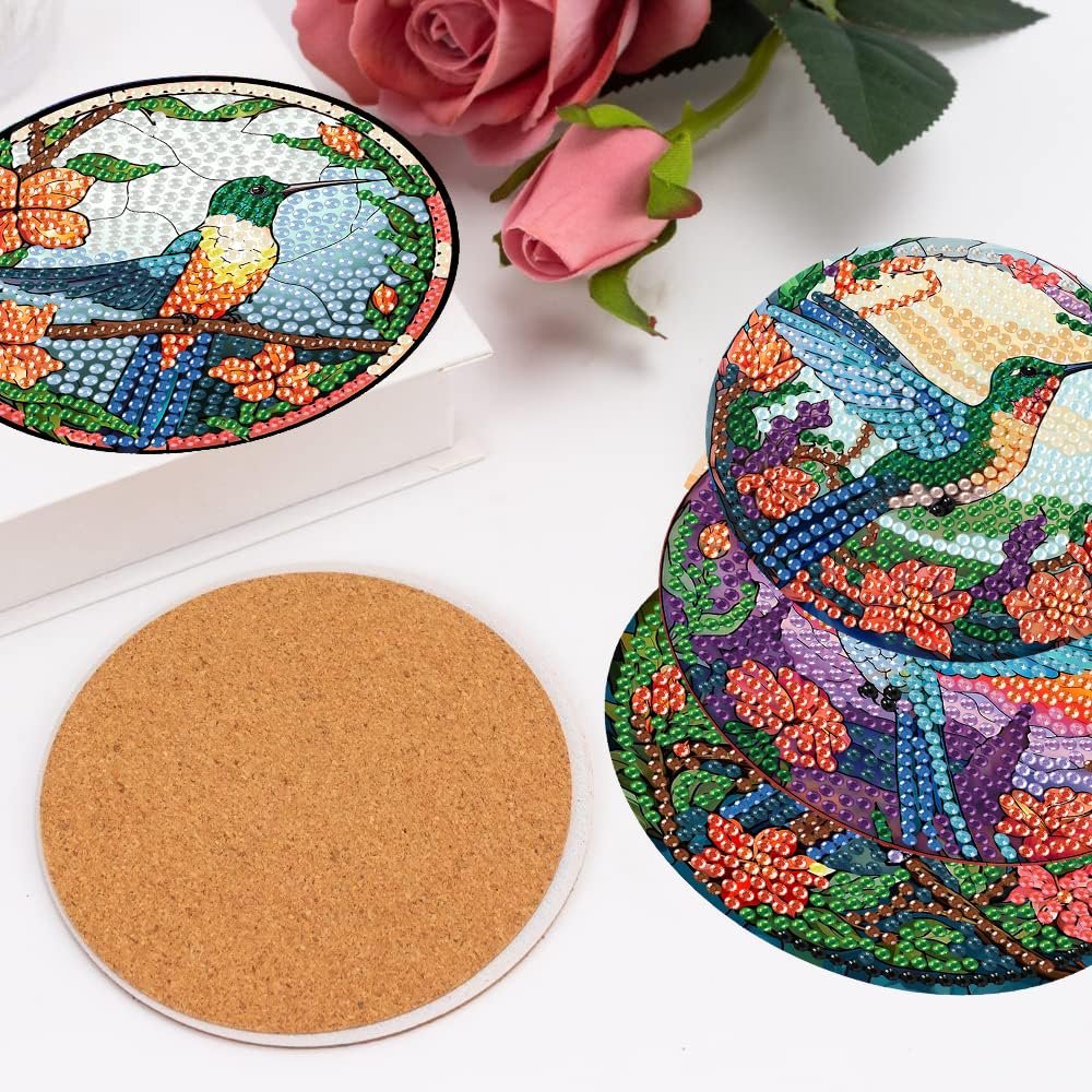 Diamond painting coasters with hummingbird designs and cork backing, displayed with roses.