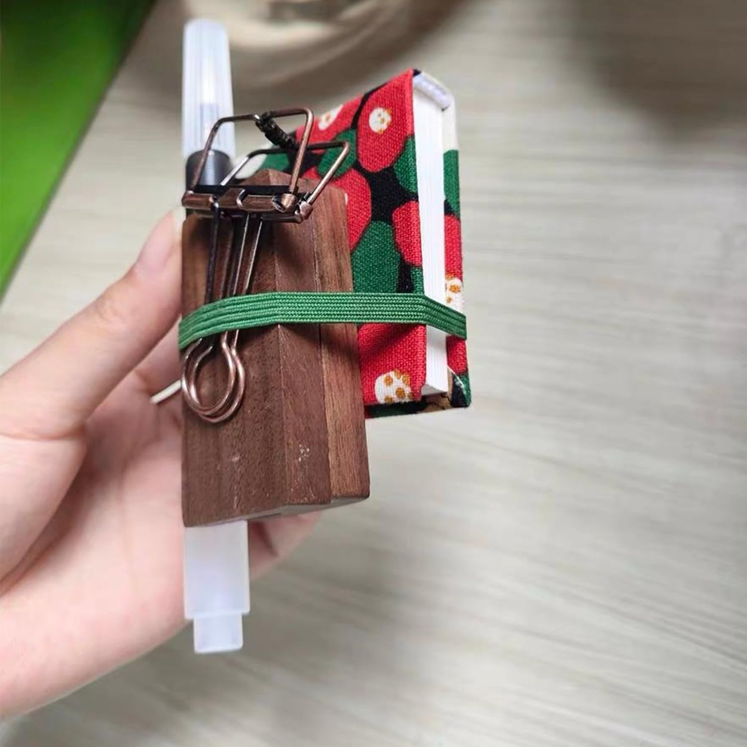 Miniature watercolor paint set with wooden block, binder clip, and small sketchbook held by a hand.