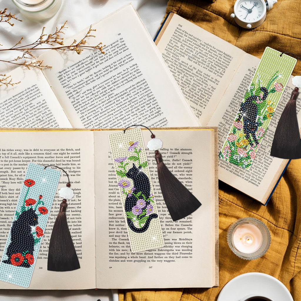 Diamond art cross bookmarks with black cats and flowers, laid on open books with tassels.