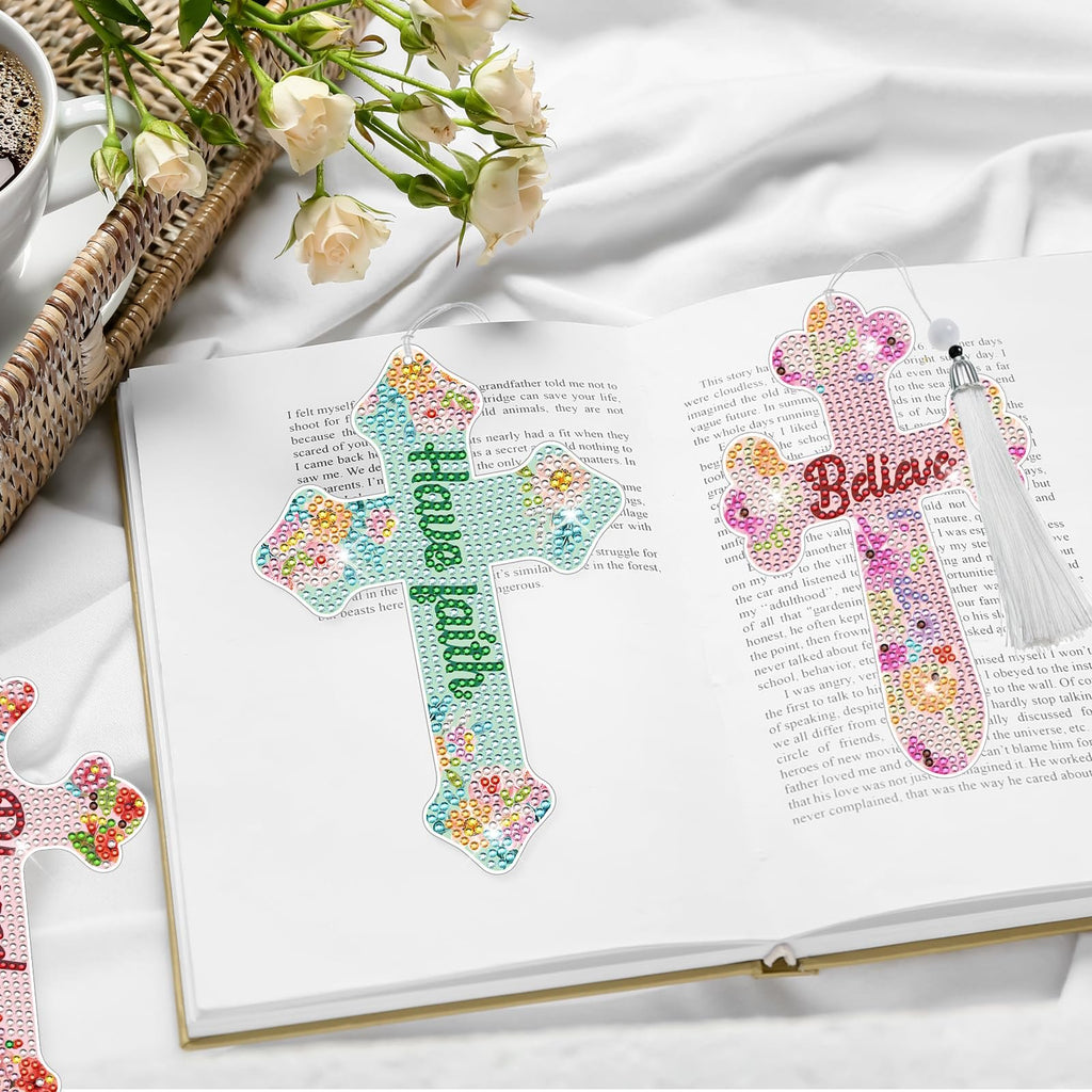 Two diamond art cross bookmarks, one reading 'Have Faith' and the other 'Believe', placed on an open book with tassels.