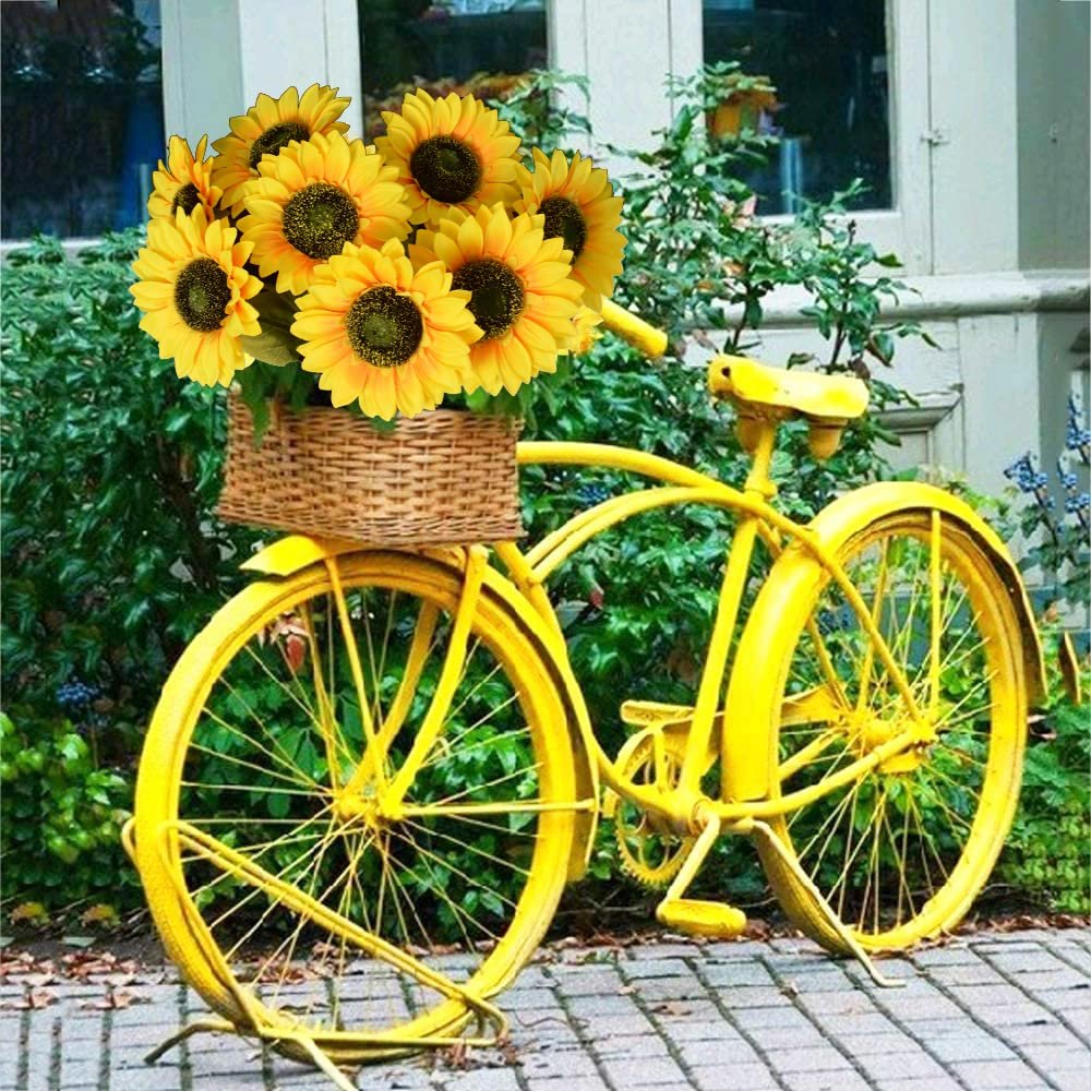 Yellow bicycle with a basket of sunflowers in front of greenery and a building.
