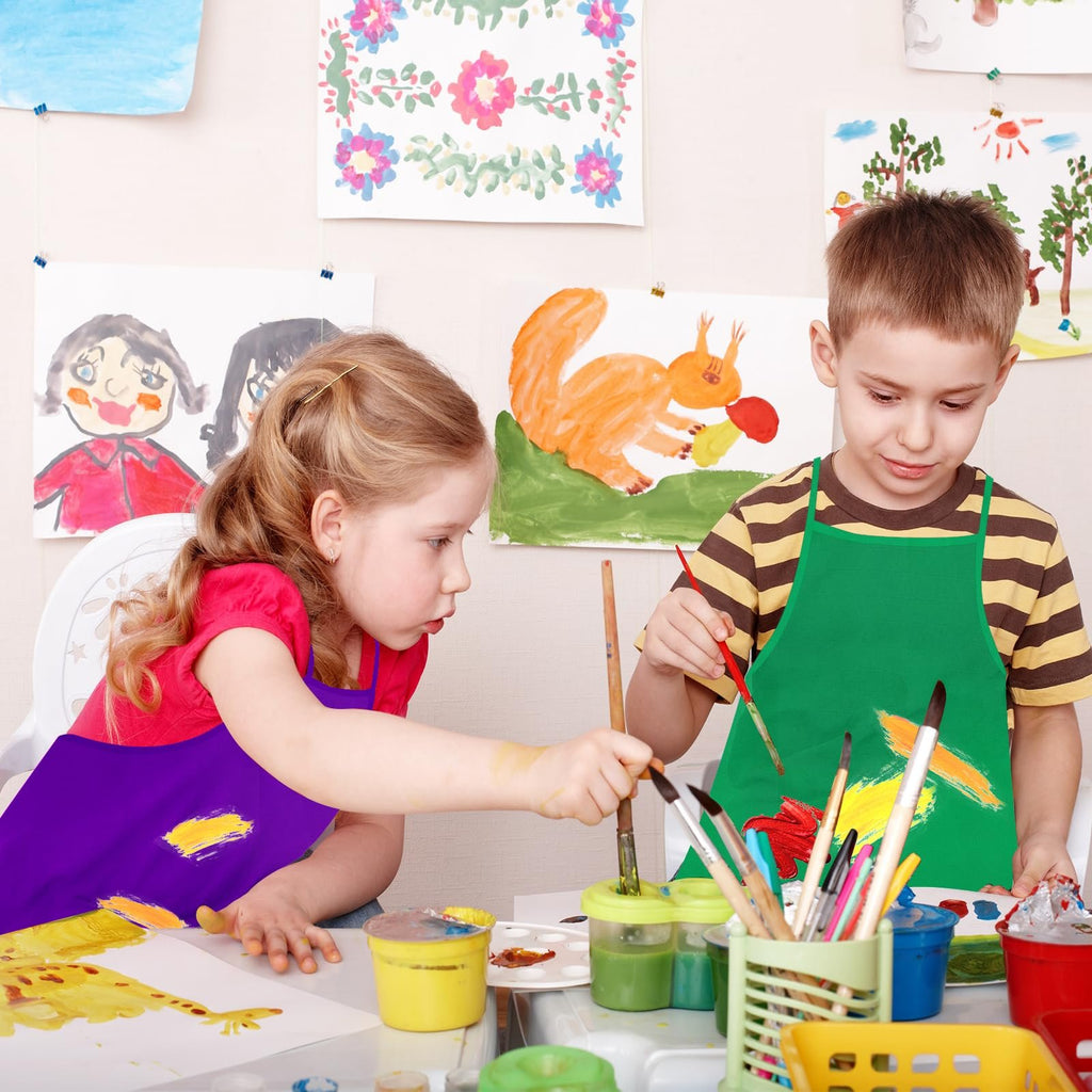 Two children painting at a table, wearing colorful aprons. Artwork is displayed on the wall behind them.