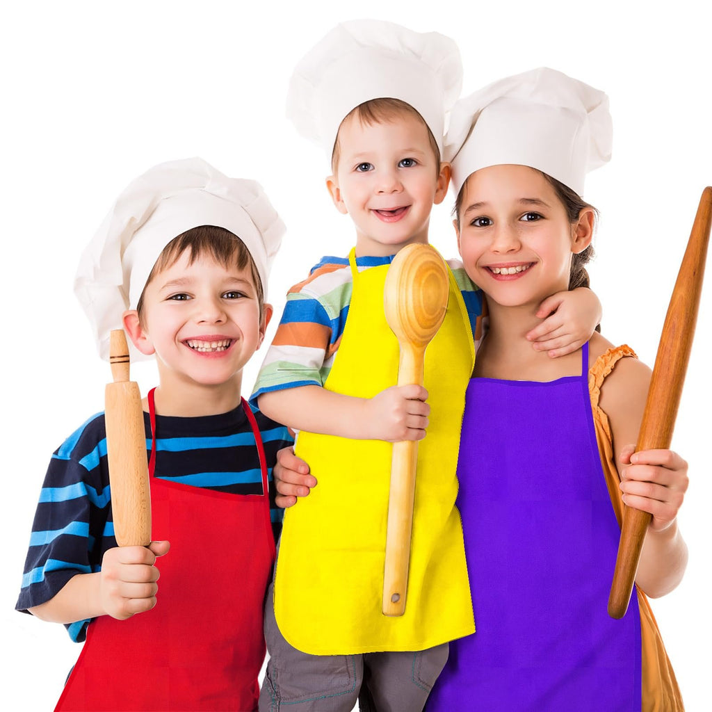 Three smiling children wearing chef hats and aprons, holding kitchen utensils like rolling pins and a wooden spoon.