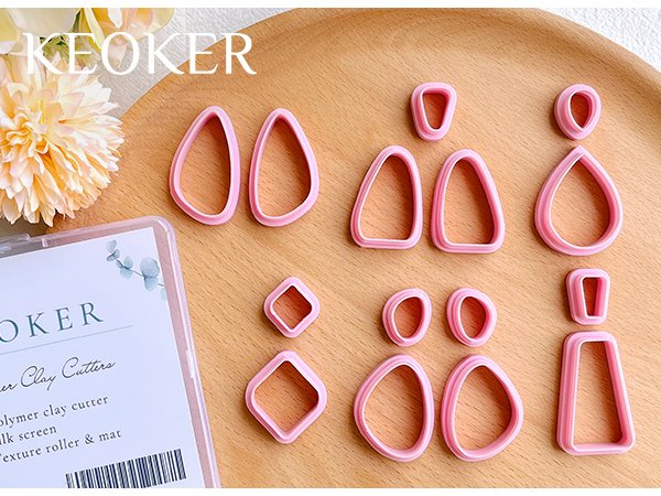 Set of pink polymer clay cutters in various geometric shapes arranged on a wooden surface with a decorative flower.