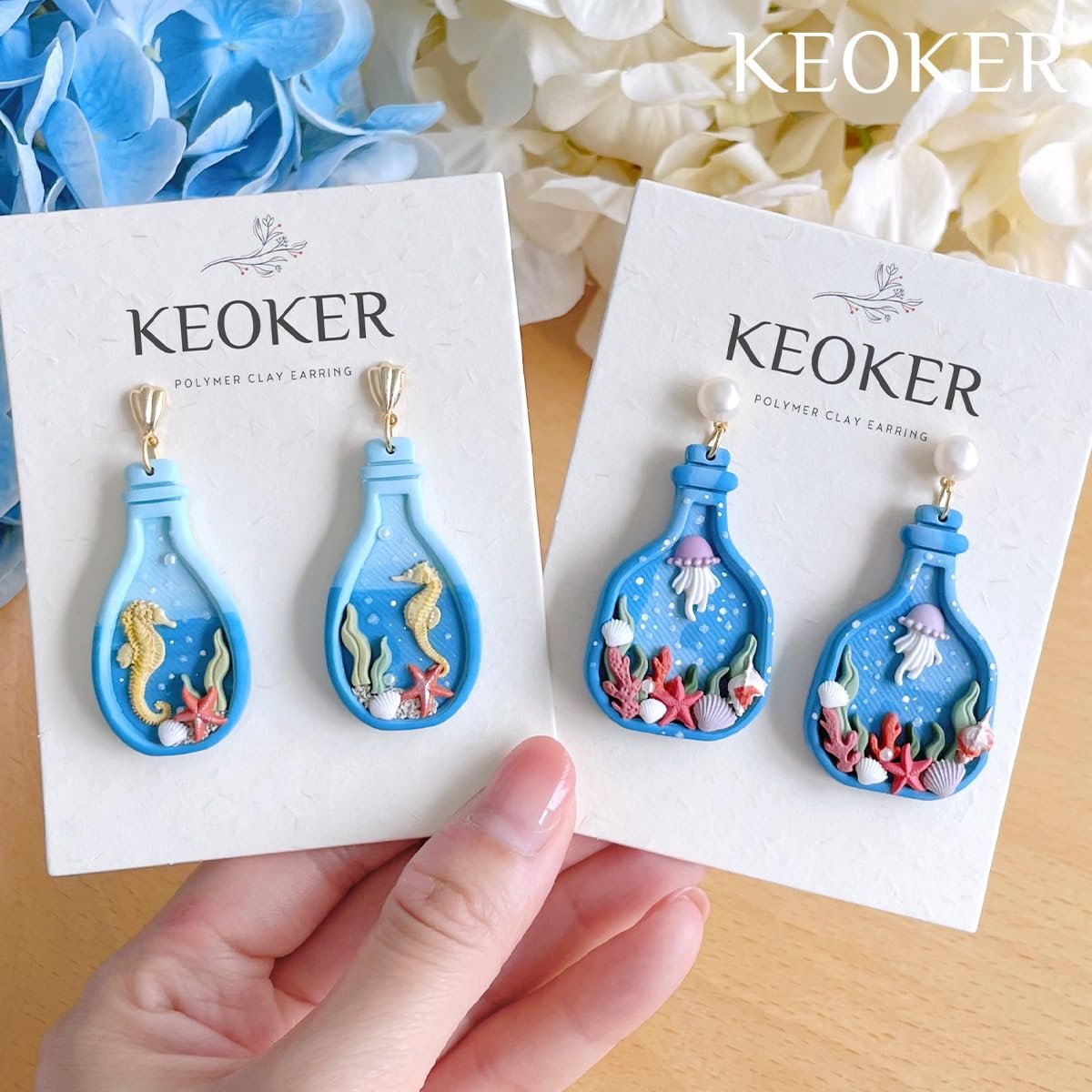 Two pairs of blue bottle-shaped polymer clay earrings with ocean scenes, held by a hand.