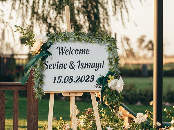 Wedding welcome sign with eucalyptus garland and flowers, displaying names and date.