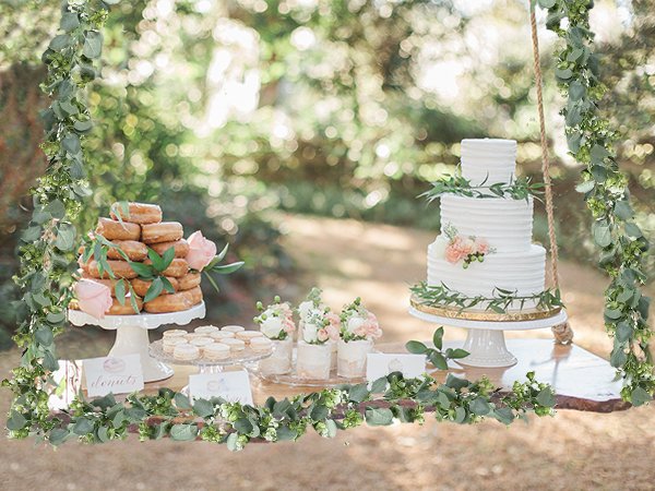 Artificial eucalyptus garland draped around a wedding dessert table with donuts and a tiered cake.