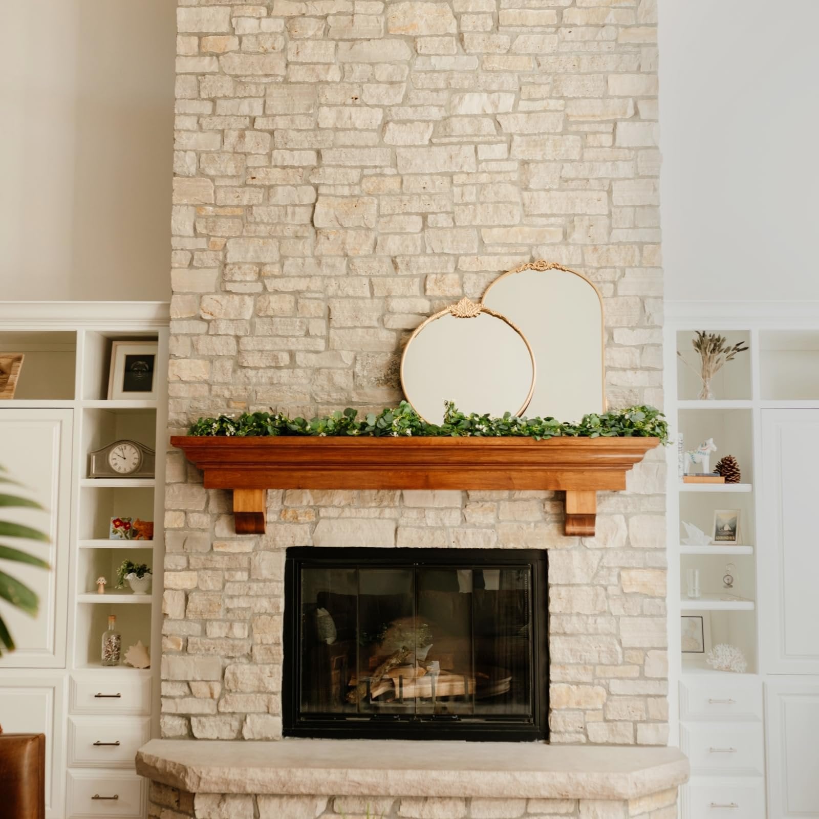 Artificial eucalyptus garland with white flowers draped over a wooden mantelpiece above a stone fireplace.