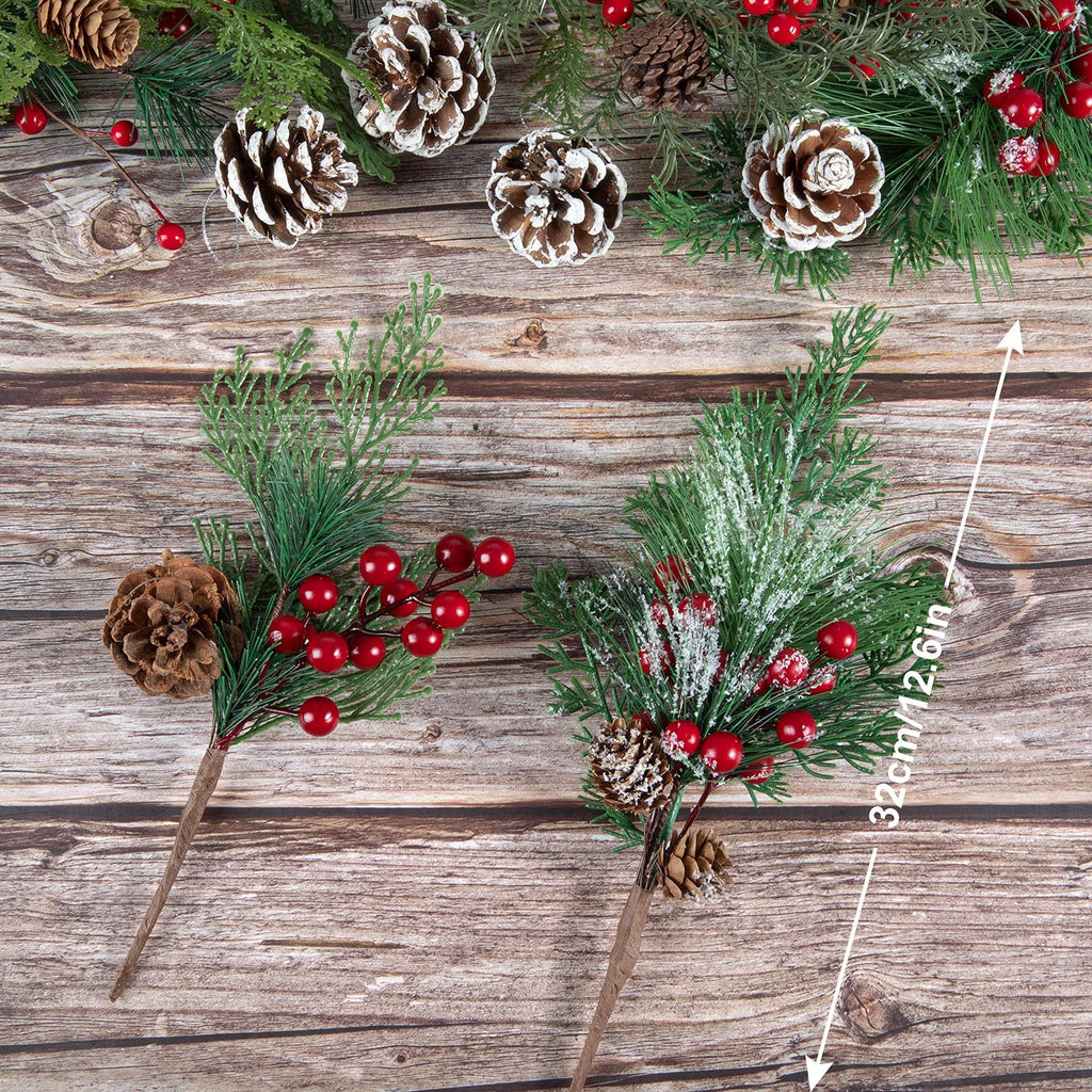 Two artificial Christmas picks with pine cones and red berries on a wooden background, one with frosted pine needles.