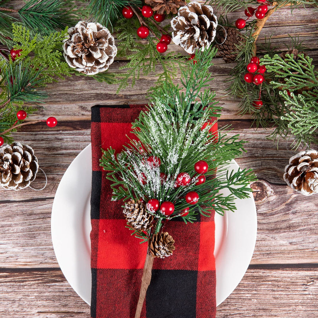Christmas pine picks with red berries and pine cones arranged on a white plate with a red and black buffalo plaid napkin.
