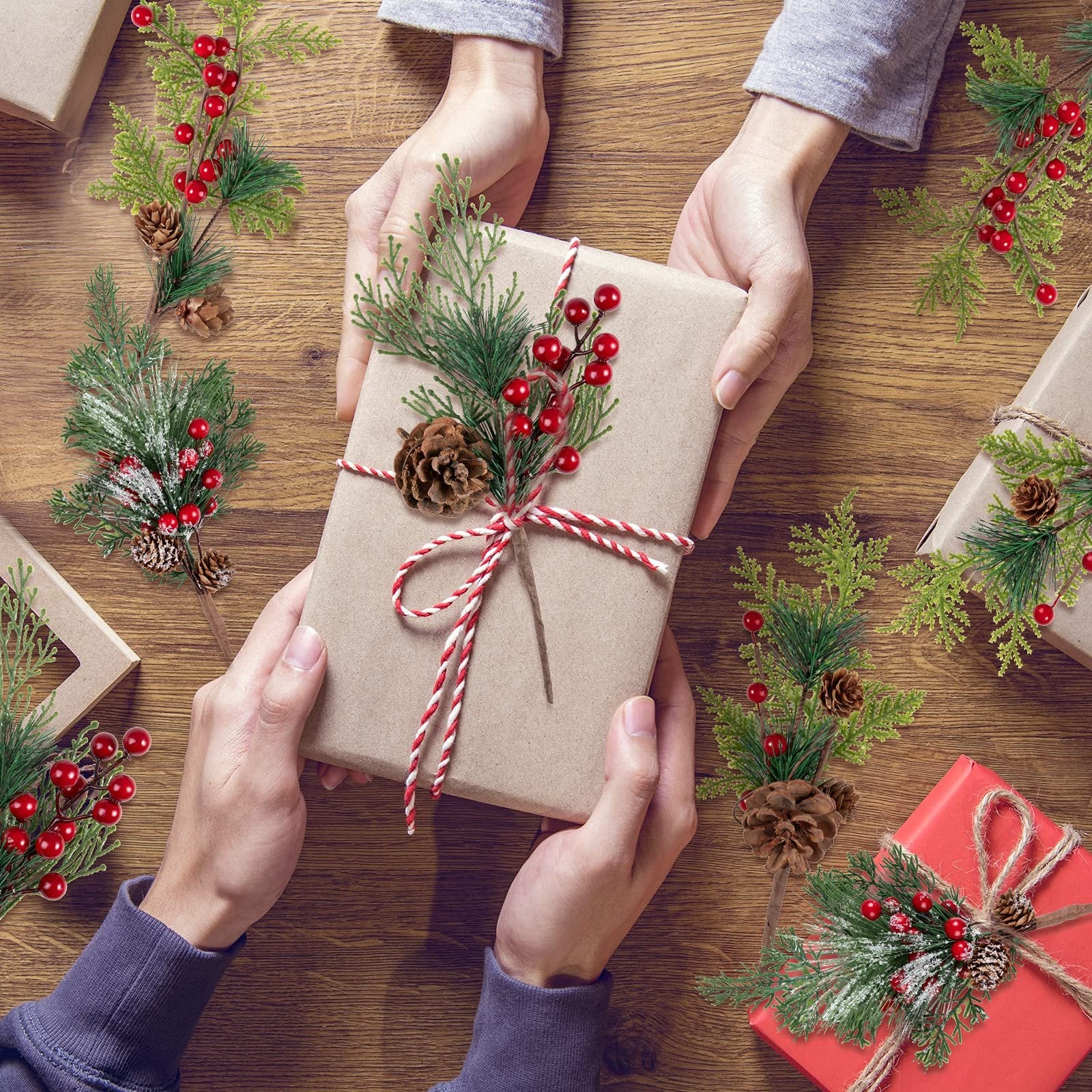 Hands exchanging a gift wrapped in brown paper adorned with artificial pine sprigs, red berries, and pine cones.