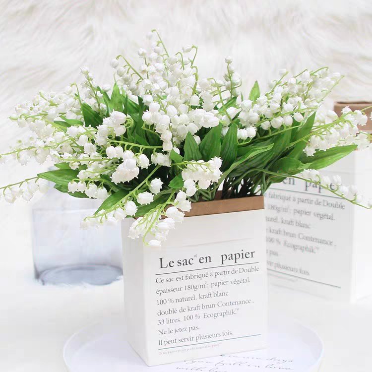 Artificial lily of the valley flowers in a white paper pot with French text